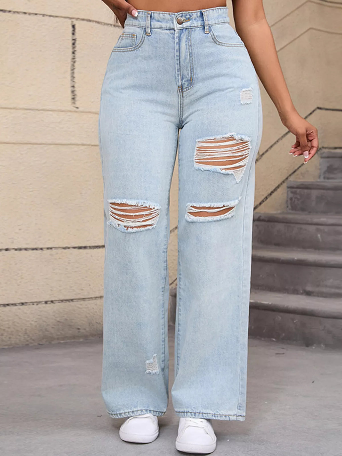 Straight-on view of pale blue distressed jeans with ripped knees and white trainers