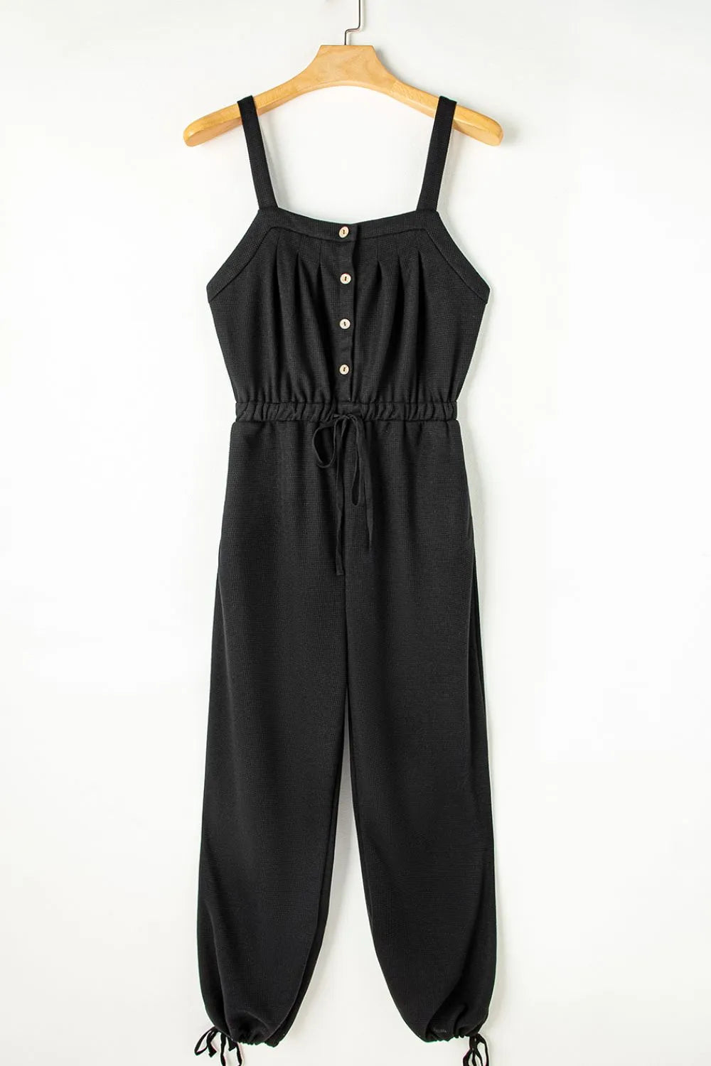 Black textured jumpsuit, front view on wooden hanger