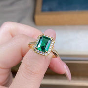 Emerald-green rectangular stone ring with a gold-tone halo worn on a hand.