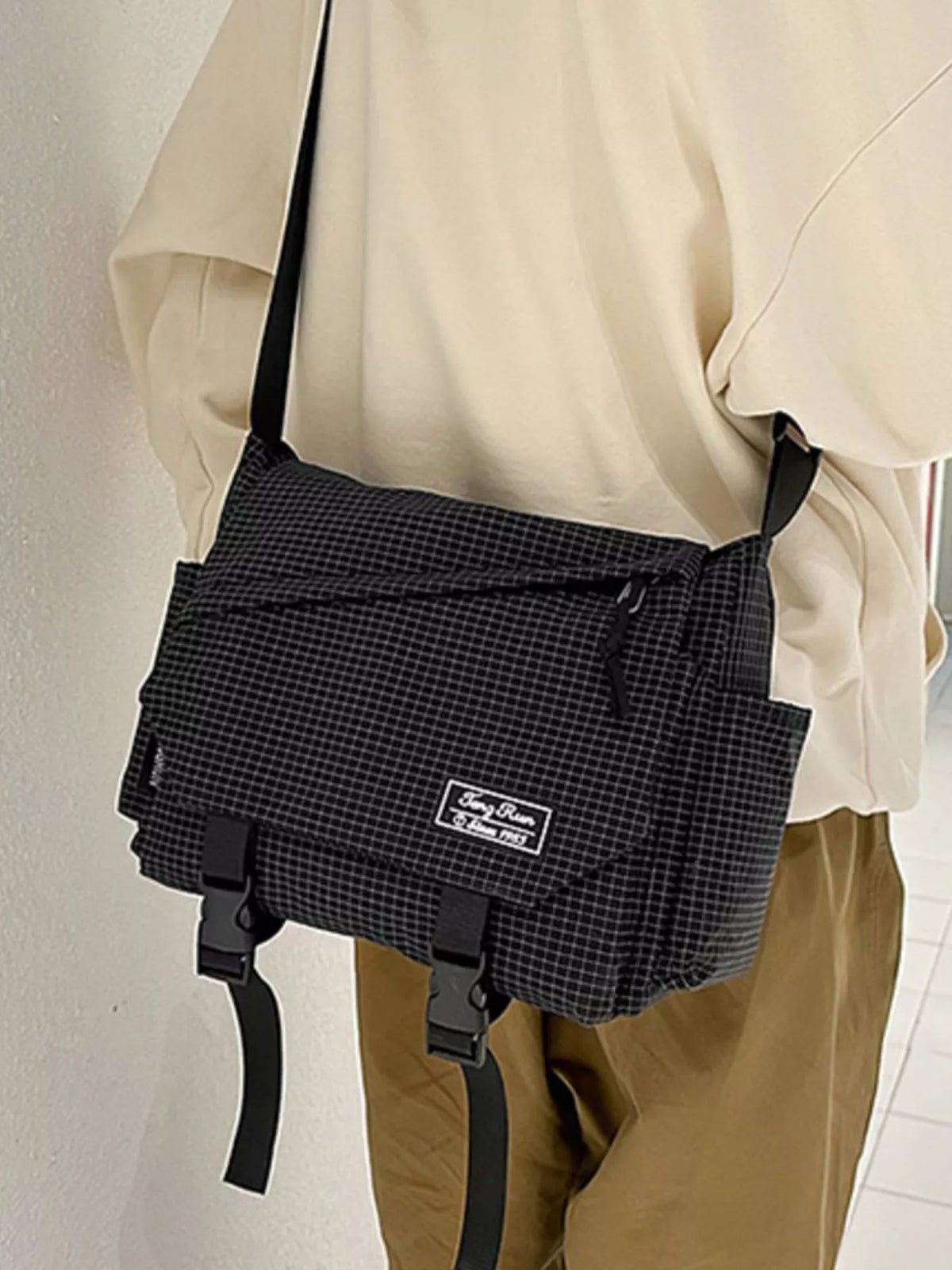 Black checked flap bag with two buckles and a diagonal zip pocket, close front view on a model