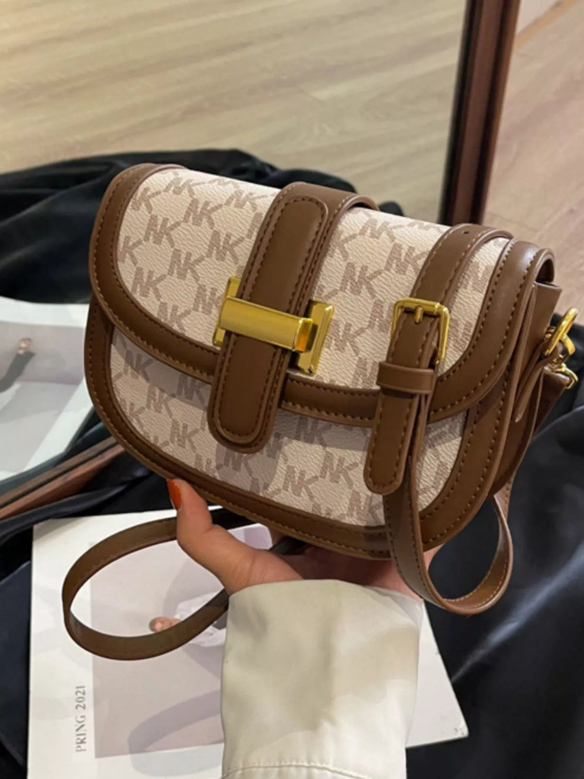 Cream and brown patterned flap bag held to show its front clasp and adjustable strap buckle