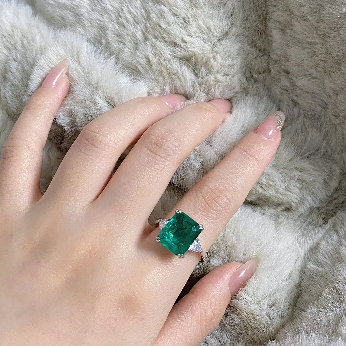 Green rectangular zircon ring worn on a hand.
