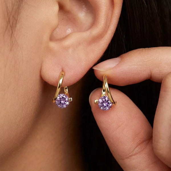 Gold-tone hoop earrings with purple round stones worn on an ear