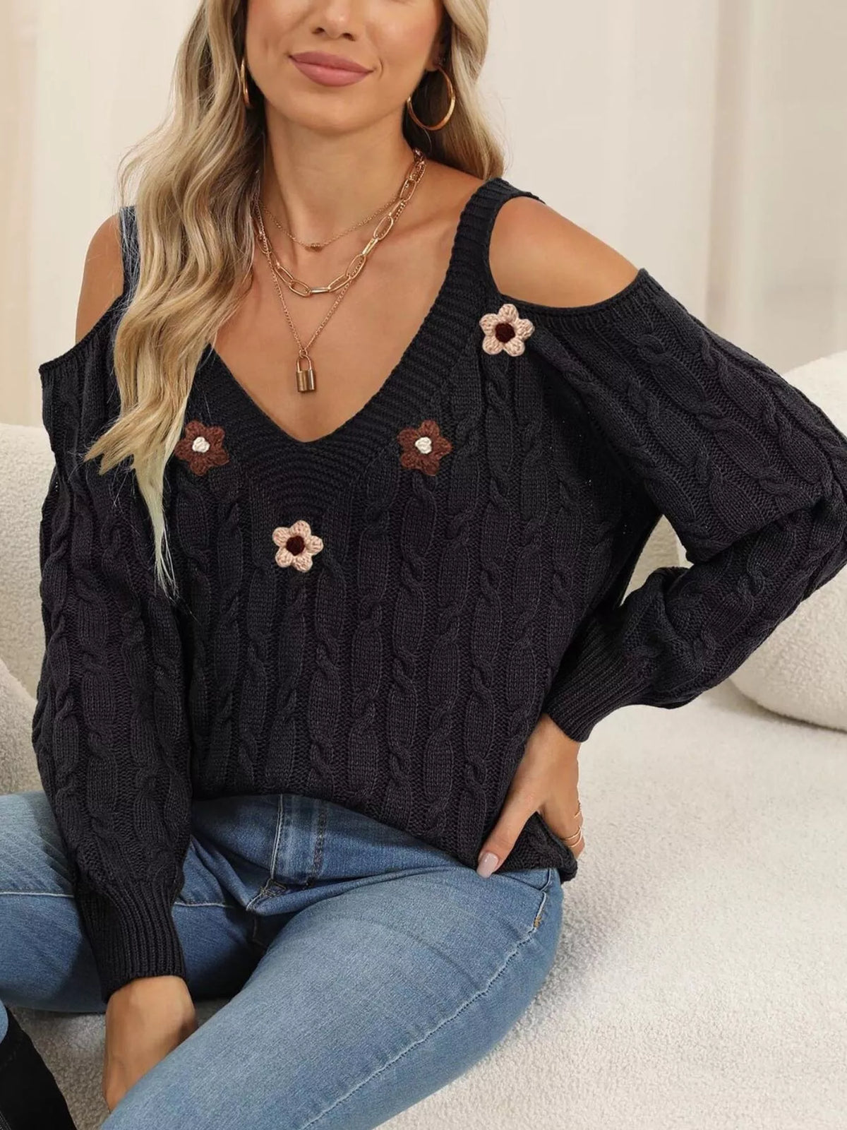 Black floral-appliqué cable-knit sweater worn with one hand at hip