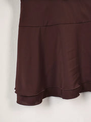 Close view of the tiered skirt seam and curved hem on the dark brown dress