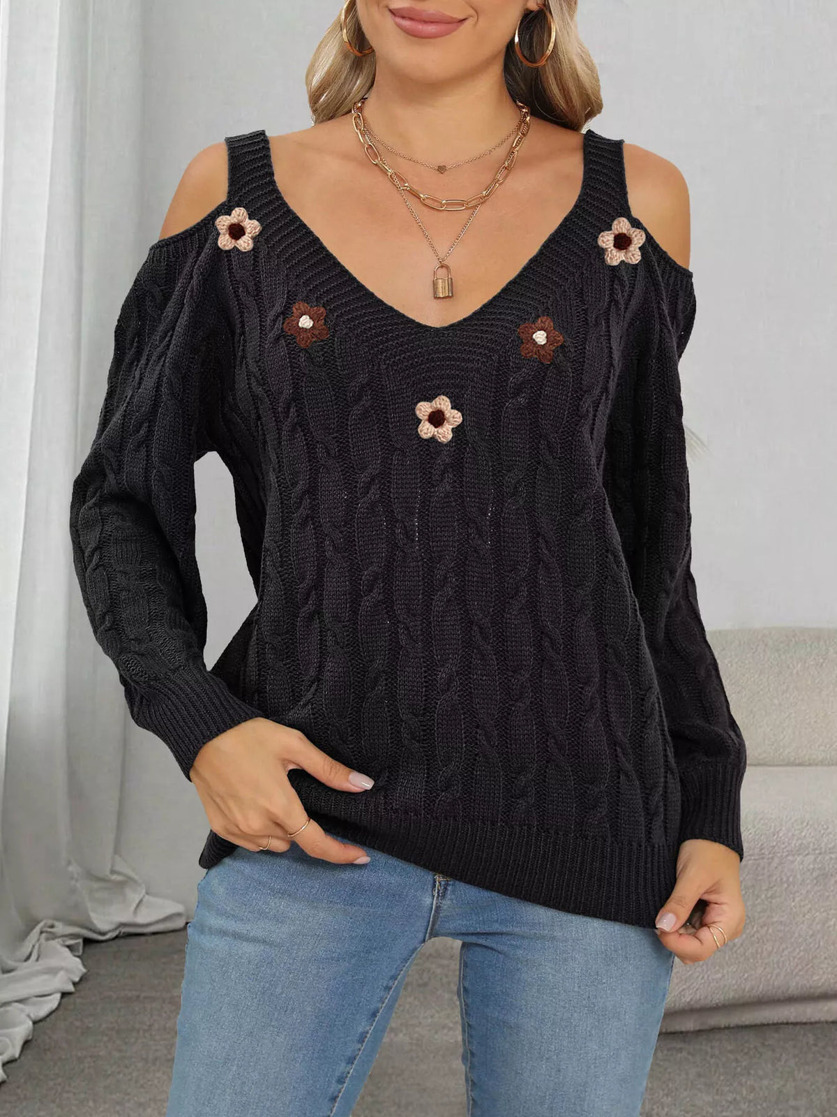Black cold-shoulder cable-knit sweater with floral appliqués, relaxed front pose