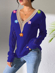Blue V-neck floral-appliqué sweater shown at an angle with a hand in a jeans pocket.
