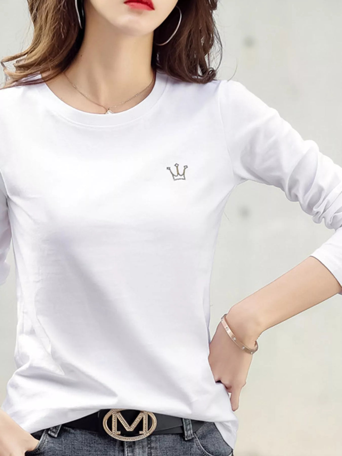 White long-sleeve T-shirt with a small crown emblem, shown on a model from the front.