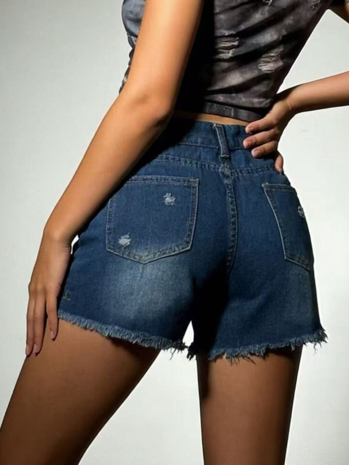 Model wearing dark-wash distressed denim shorts