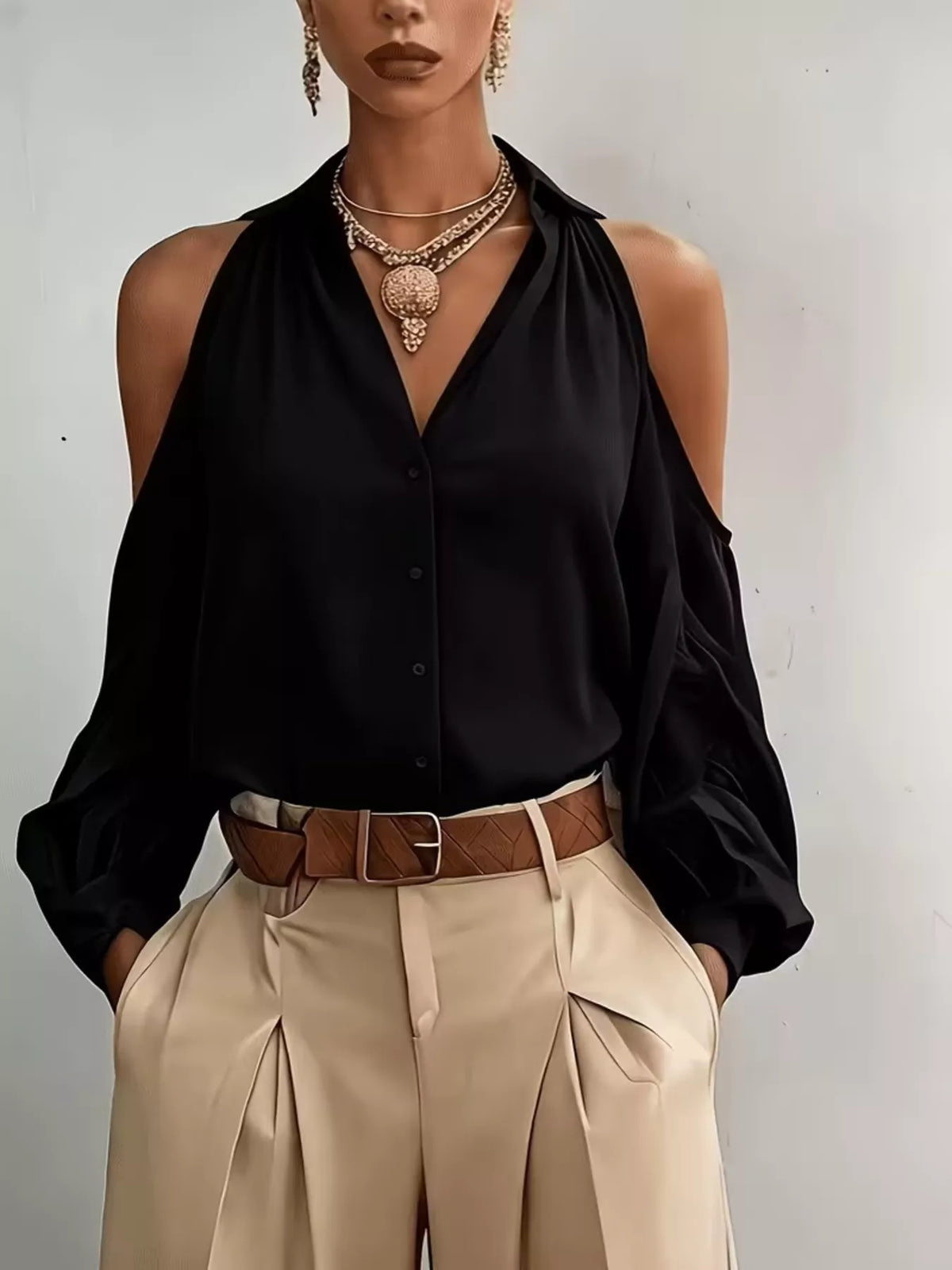 Model wearing a black cold-shoulder blouse with a draped neckline and beige trousers.