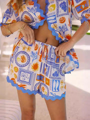 Front view of matching printed button-up shirt and shorts with orange scalloped trim.