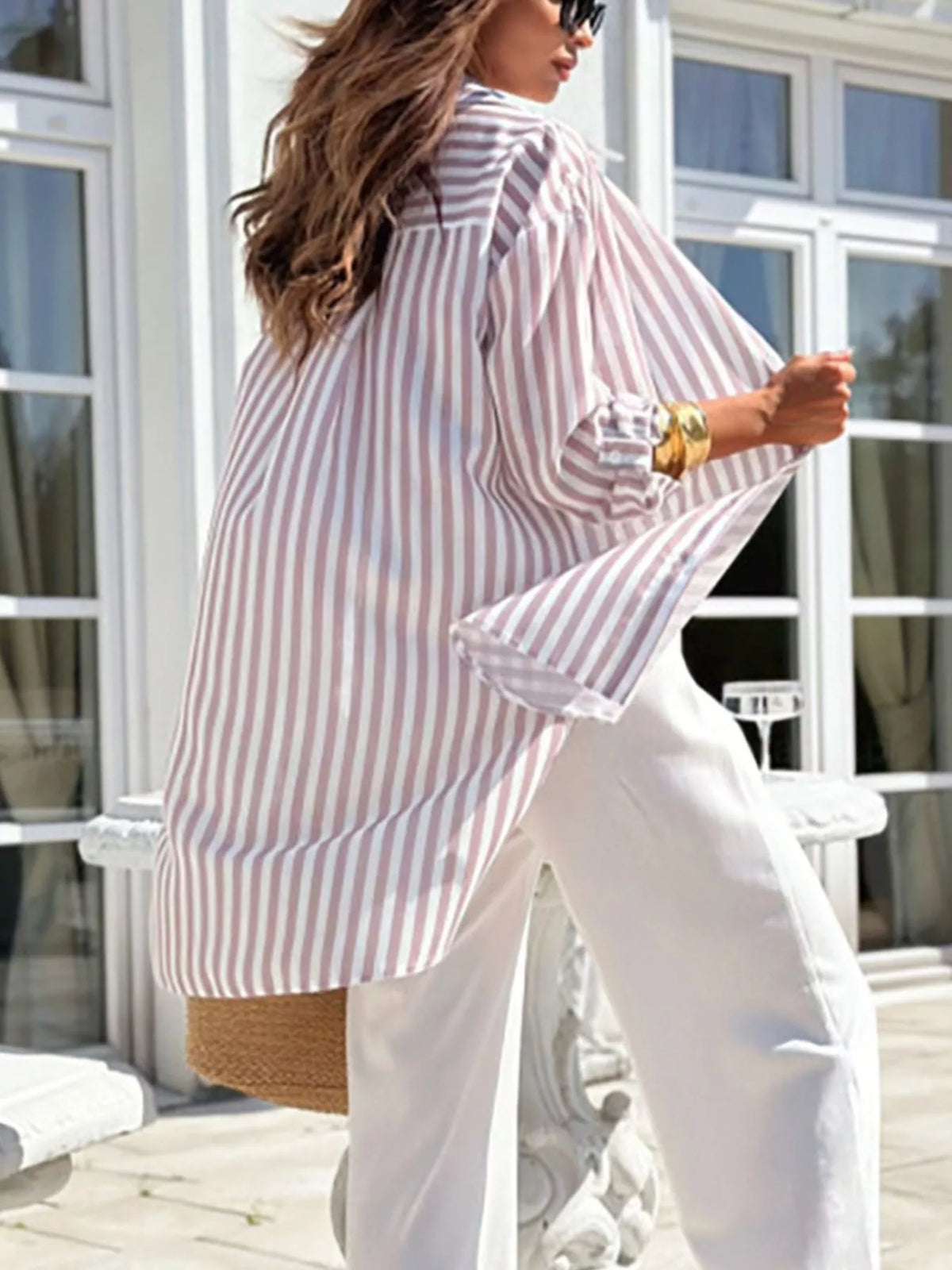 Back view of blue striped oversized shirt worn with white trousers.